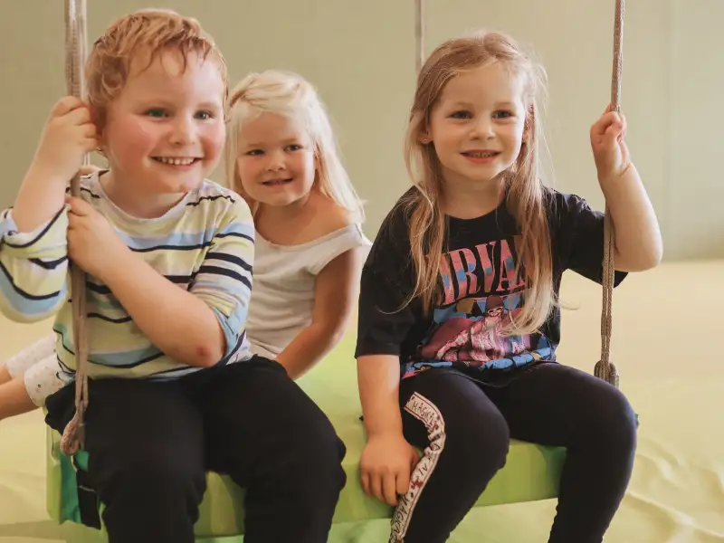 Drei Kinder sitzen gemeinsam auf einer großen Schaukel.