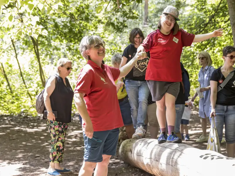 Eineinklusive Gruppe im Wald, junge Leute balancieren auf einem Baumstamm