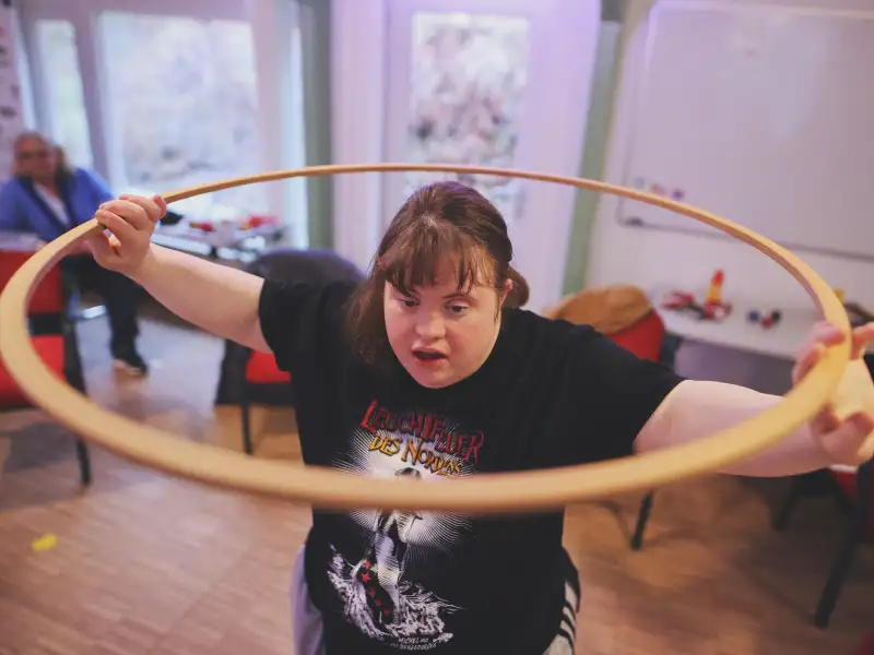 Junge Frau mit Downsyndrom hebt einen Hula-Hoop-Reifen hoch