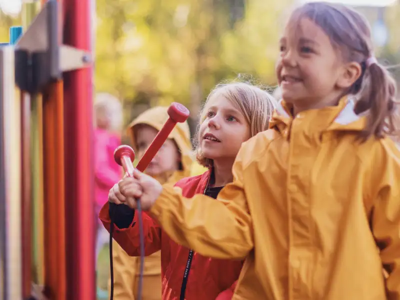 Mehrere Kindergartenkinder spielen draußen mit einem Klanginstrument