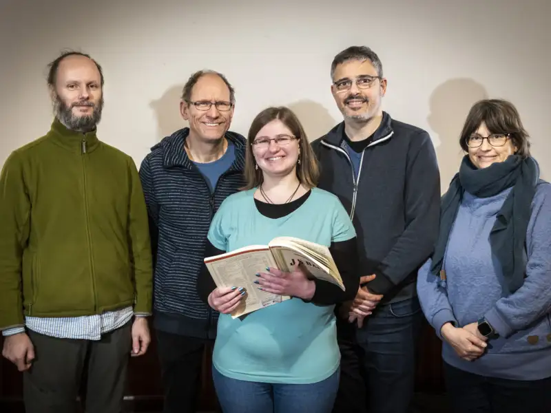 Fünf Personen lächeln in die Kamara. Eine von ihnen hat ein aufgeschlagenes Notenbuch in der Hand.
