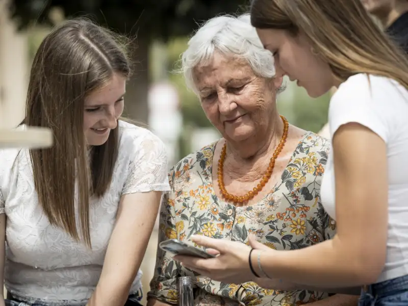 Zwei jüngere und eine ältere Frau schauen auf ein Smartphone