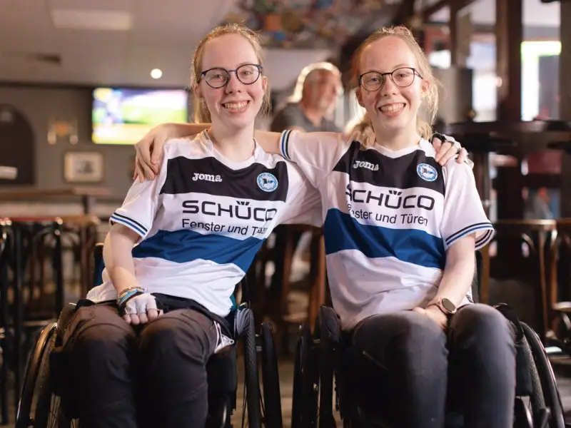 Jugendliche Zwillingsschwestern im Rollstuhl mit Fan-T-Shirts