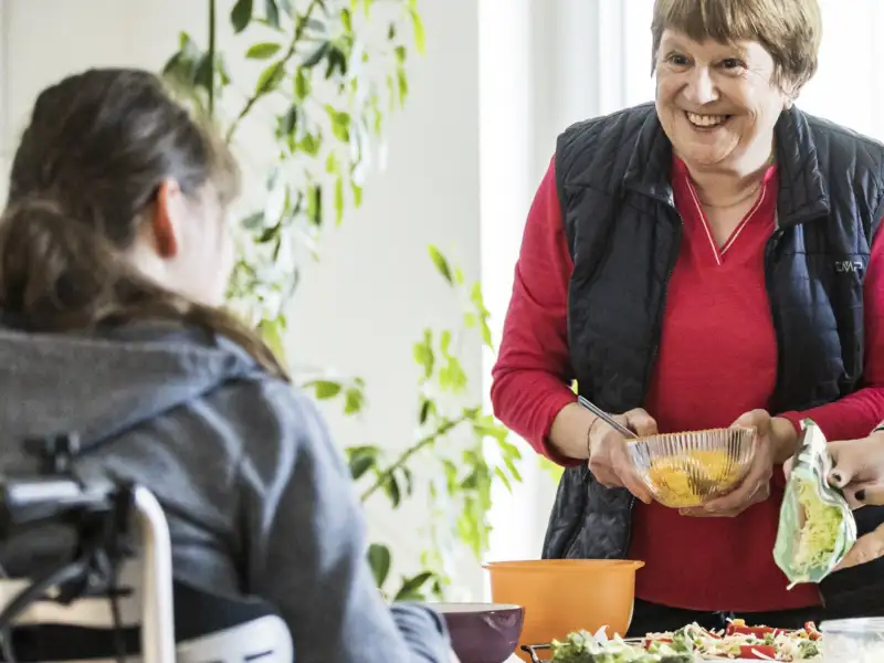 Mehrere Personen stehen und sitzen rund um einen Tisch in einer Wohnung