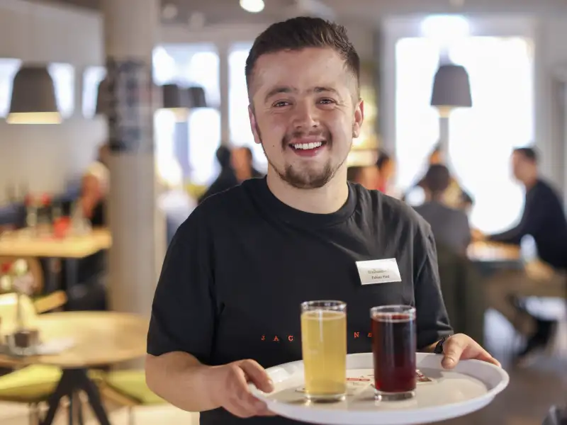 Ein Mitarbeiter eines Cafés trägt ein Tablett mit Getränken