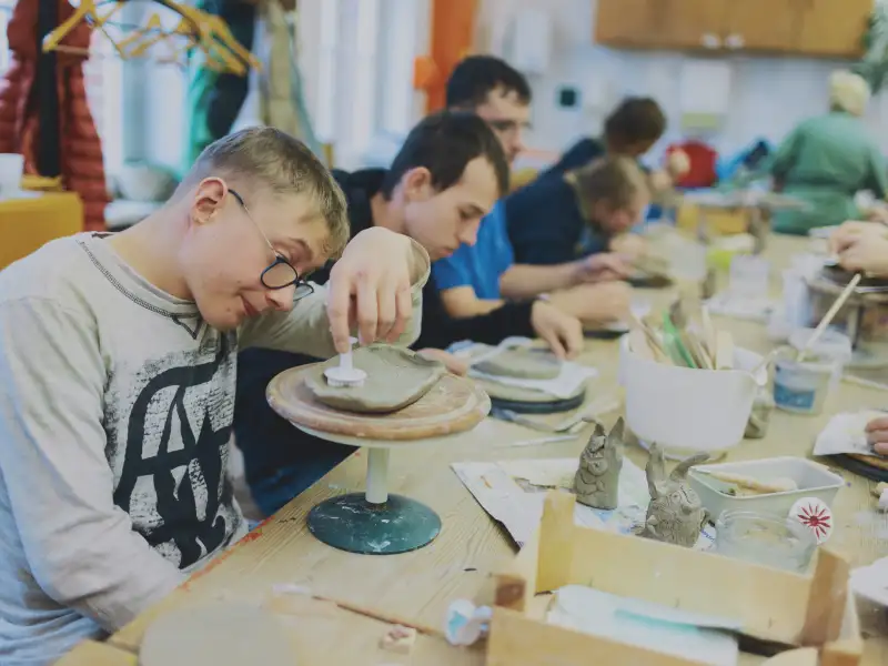 Menschen sitzen um einen Tisch und arbeiten mit Ton