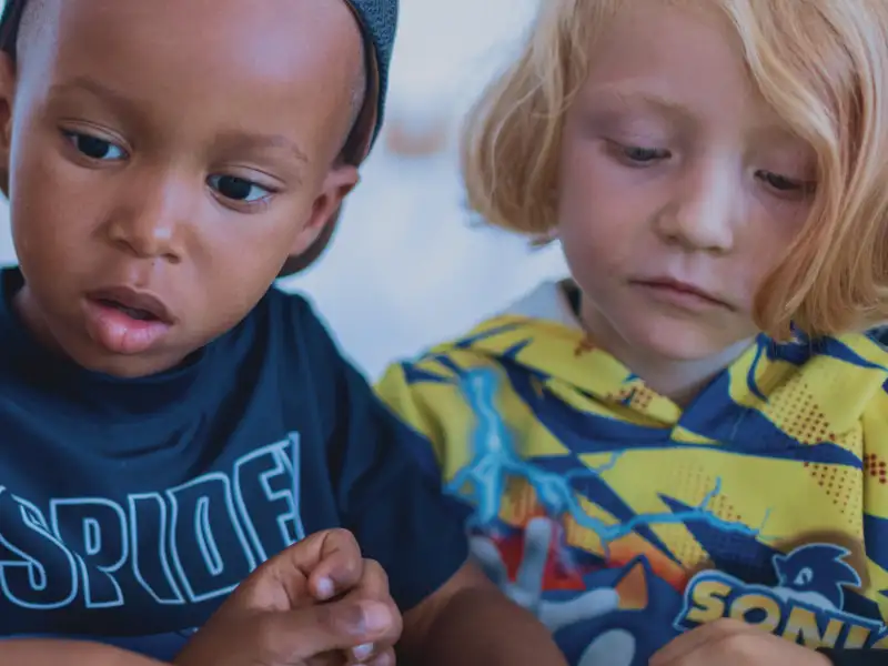 Zwei dunkelhäutige und ein blonder Junge im Kindergartenalter. Einer von ihnen schneidet einen Apfel in Stücke.