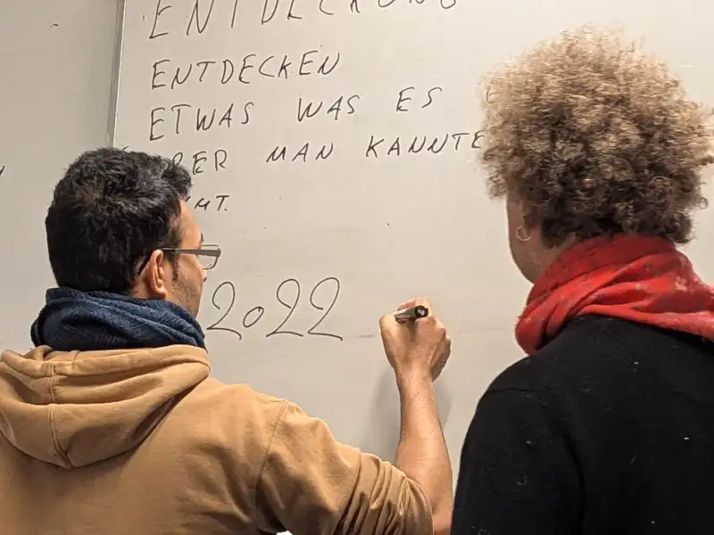Eine Frau steht neben einem Mann, der Zahlen auf ein Flipchard schreibt.