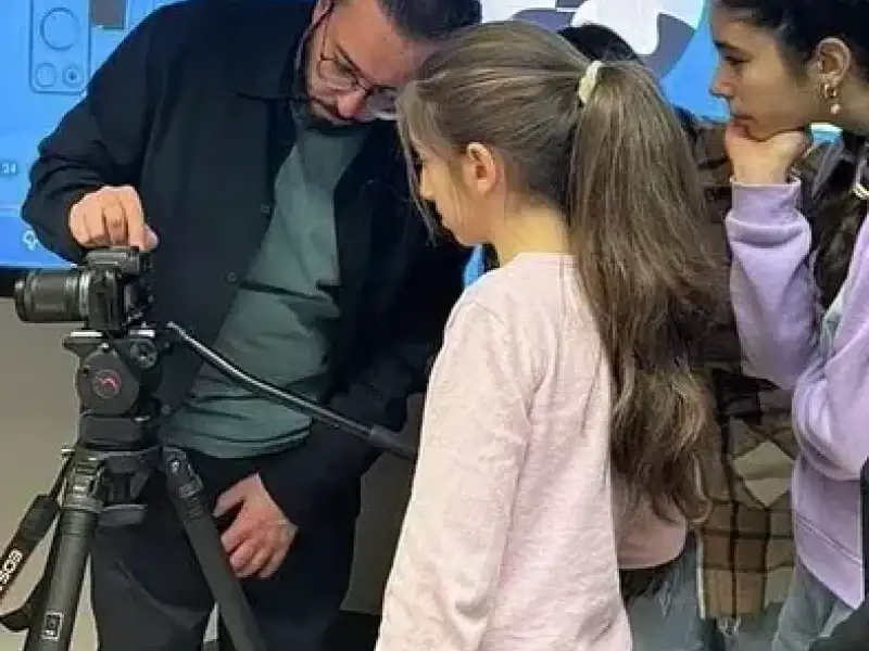 Ein Mann erklärt einer Gruppe von Kindern eine Fotokamera auf einem Stativ.