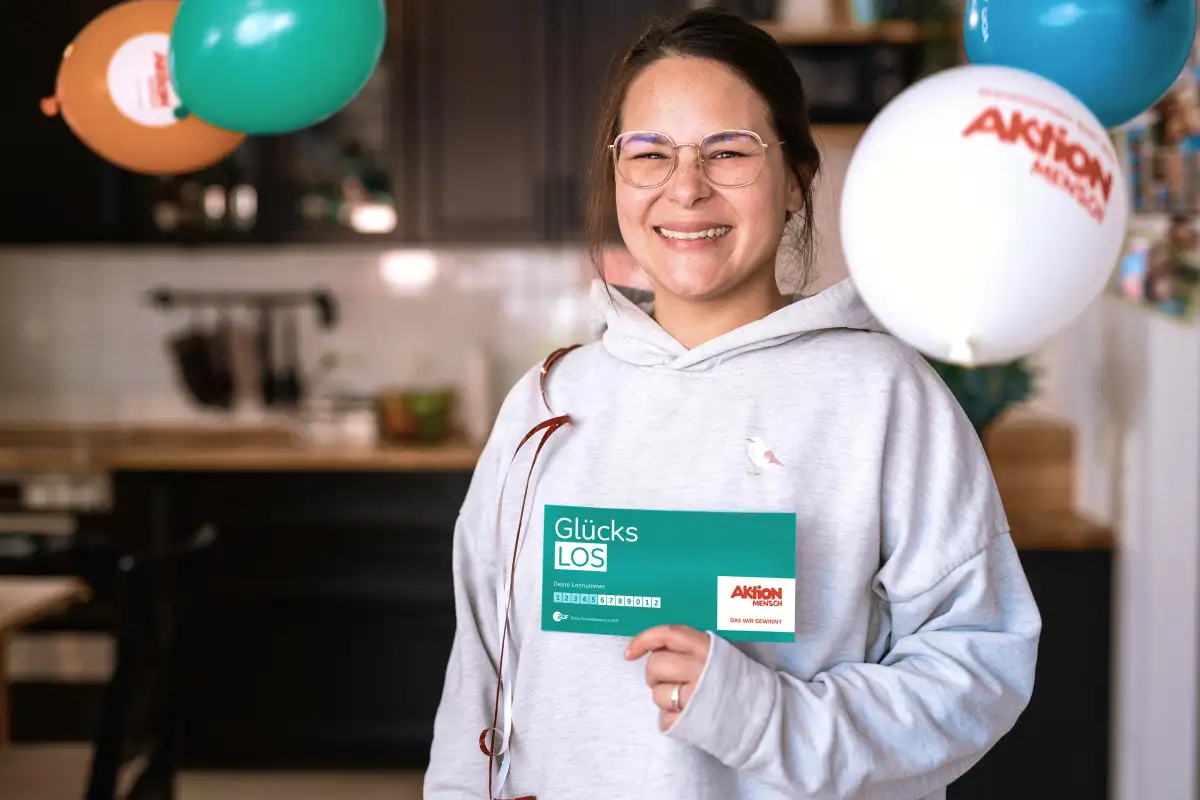 Junge Frau hält freudestrahlend ihr Glückslos in der Hand und freut sich über ihren Gewinn.