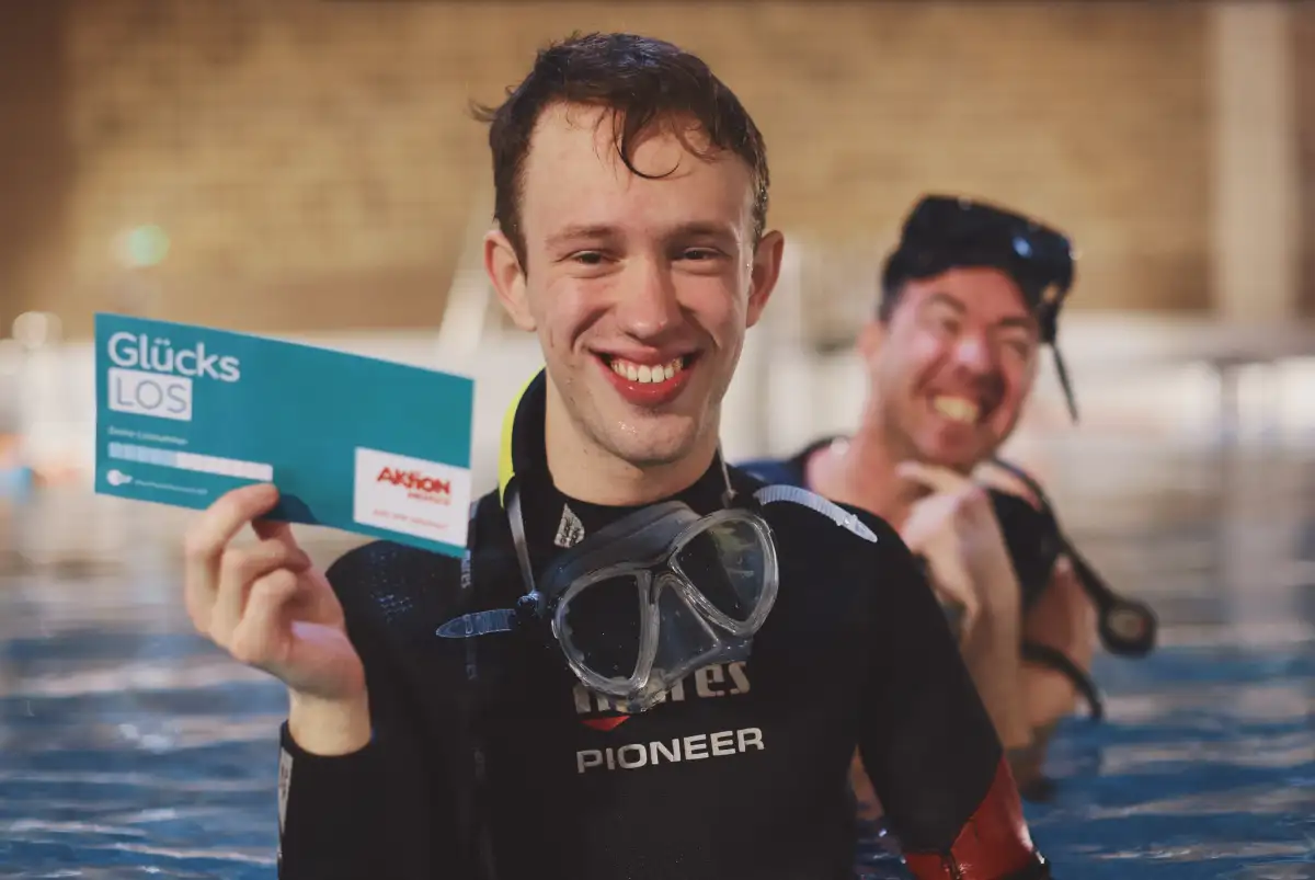 Gewinner Mika erfährt wie sein Glückslos beiträgt den inklusiven Tauchsport in Köln Pulheim zu ermöglichen.