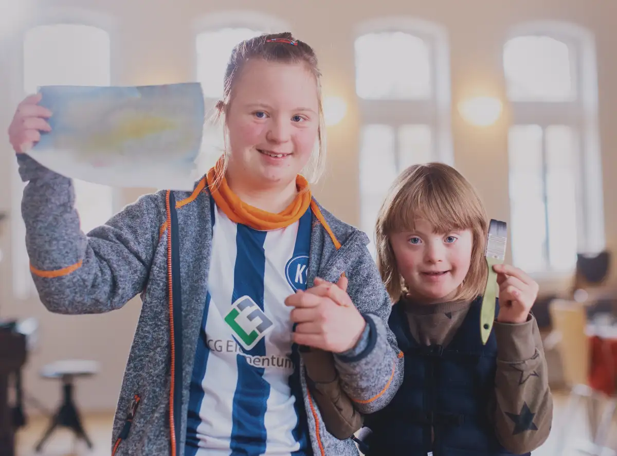 Zwei Mädchen mit und ohne Behinderung zeigen Freude strahlend ihr kreatives Werk