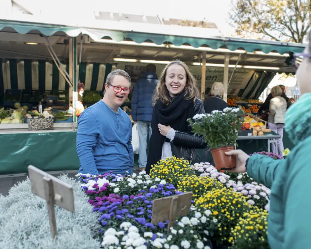 Ein junger Mann mit Downsyndrom und eine junge Frau schauen sich Blumen auf einem Markt an.