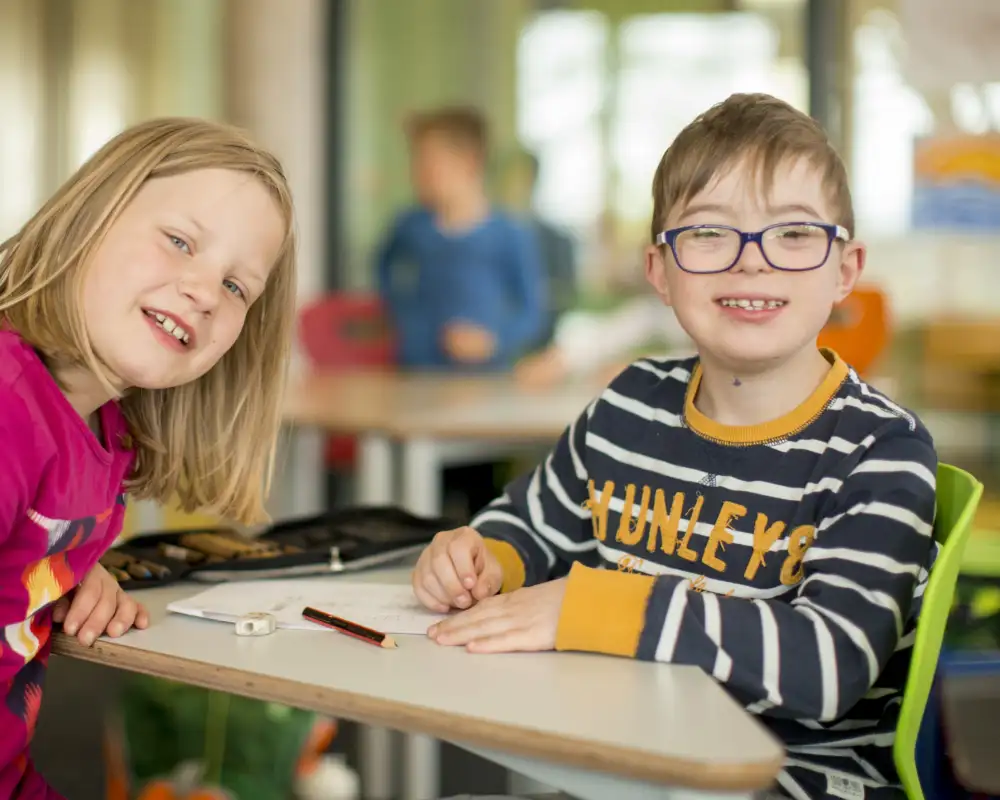 Ein Junge mit Behinderung und Mädchen in der Schule lächeln in die Kamera