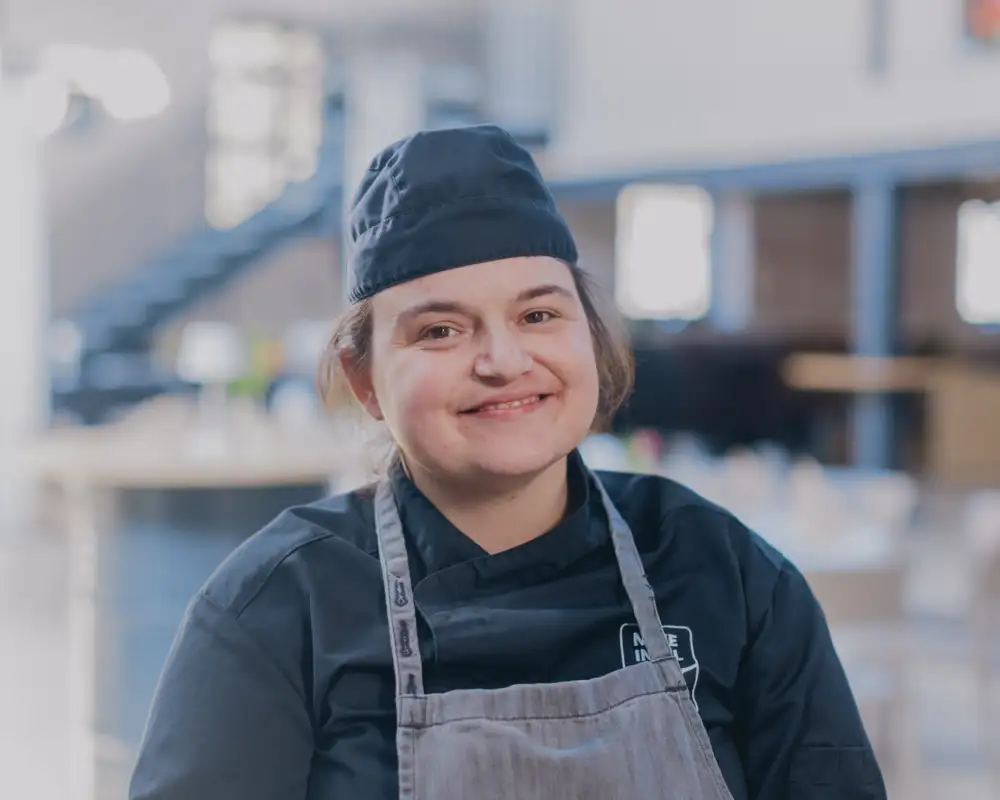 Eine junge Frau in Arbeitskleidung lächelt in die Kamera