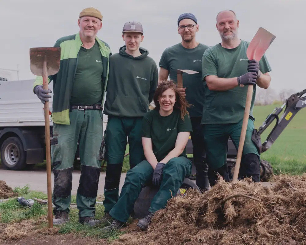 Fünf Menschen mit und ohne Behinderung in Garten-Arbeitskleidung mit Schaufeln in der Hand.