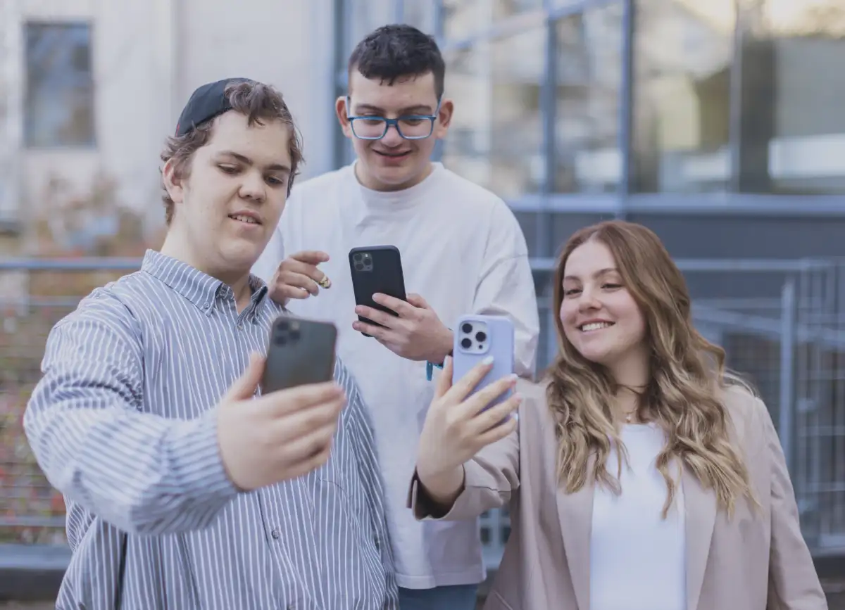 Drei junge Menschen schauen interessiert auf ihre Smartphones.