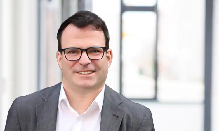 Matthias Tobies, ein Mann mit kurzen braunen Haaren und dunkler Brille, trägt einen Anzug und schaut in die Kamera.