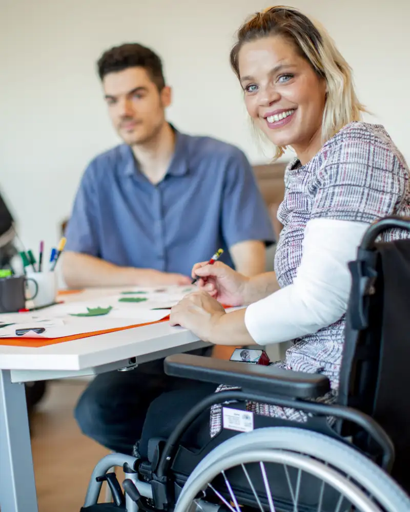 Menschen mit und ohne Behinderung sitzen an einem Tisch und arbeiten.
