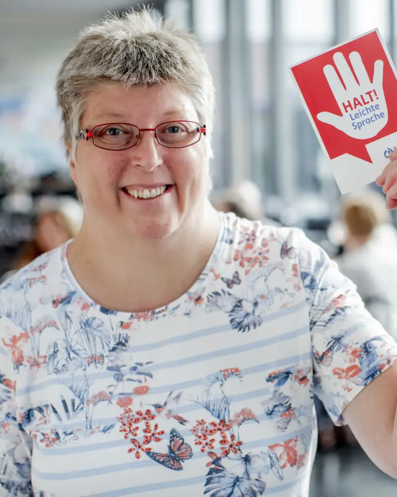 Eine Frau hält ein Schild hoch auf dem "Halt. Leichte Sprache!" steht.