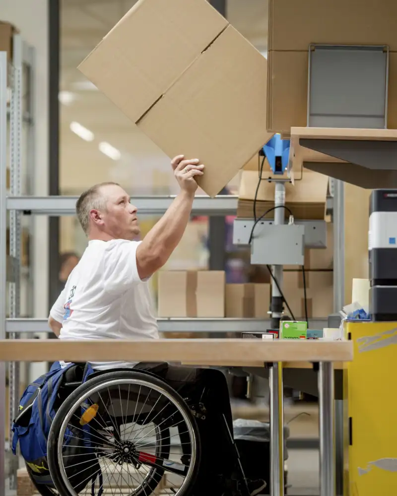 Ein Mann im Rollstuhl arbeitet in einem Verpackungsunternehmen.