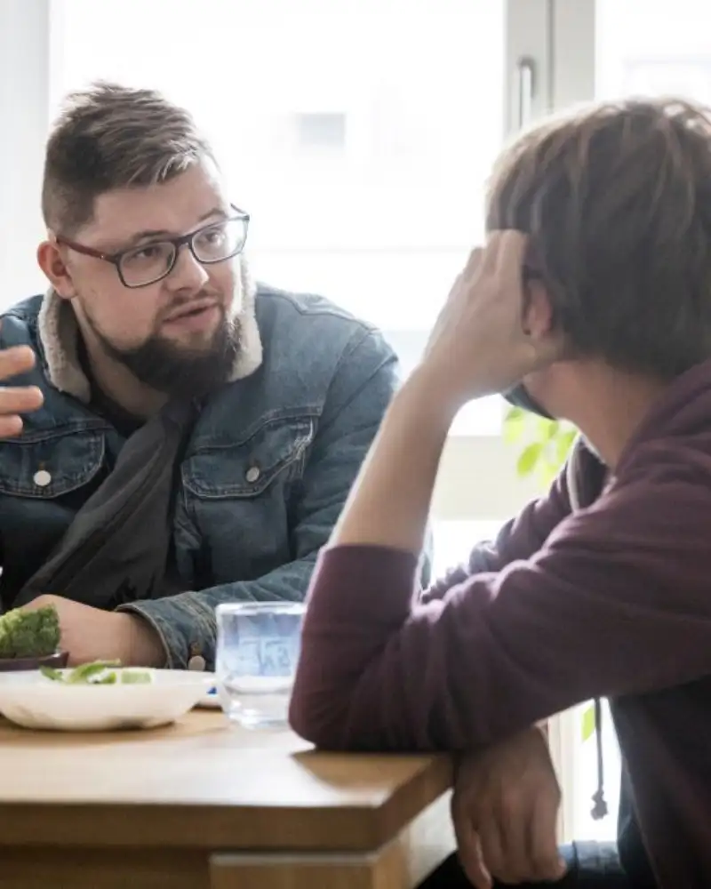 Zwei Männer sitzen an einem Tisch und sprechen miteinander.