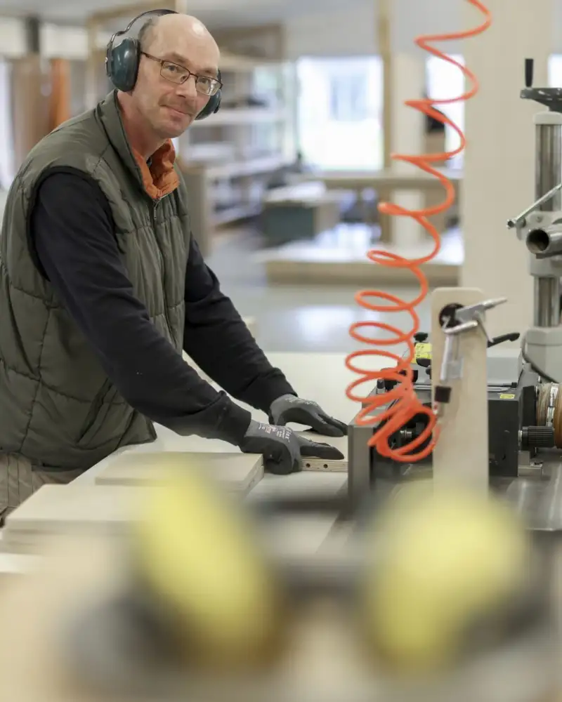 Ein Mitaarbeiter bei der maschinellen Bearbeitung von Holzbauteilen in der inkusiven Möbeltischlerei Hand in Hand-Werk Munster.