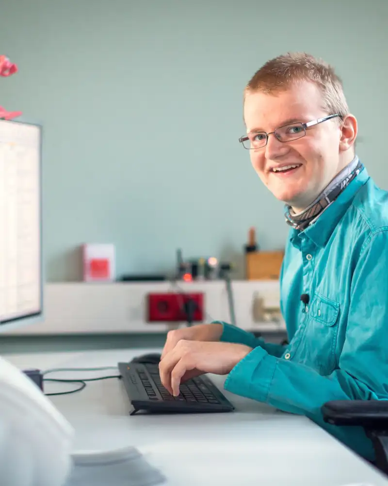 Ein junger Mann im Rollstuhl arbeitet am Computer