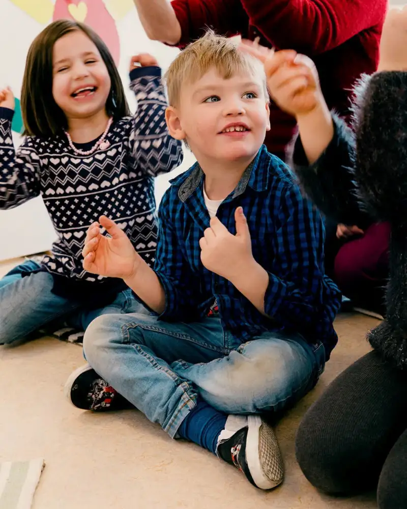 Ein Mädchen und ein Junge im Vorschulalter sitzen auf dem Fußboden und lachen.