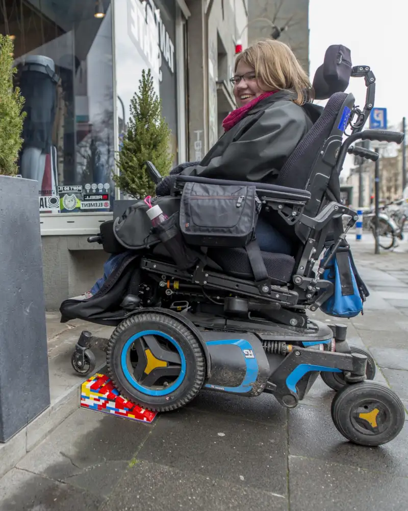 Eine Frau im E-Rolli fährt über eine Lego-Rampe in ein Geschäft.