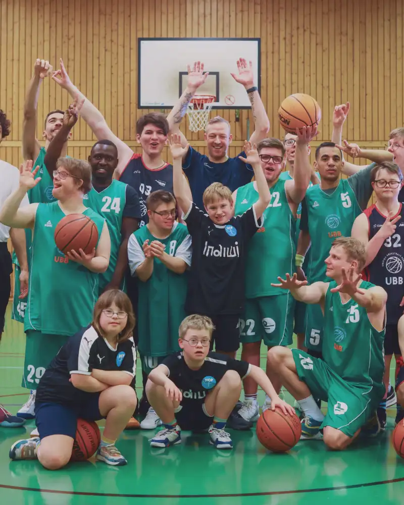 Eine inklusive Basketball-Mannschaft hebt die Hände in die Luft.