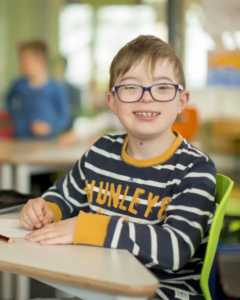 Ein Junge mit Behinderung und Mädchen in der Schule lächeln in die Kamera