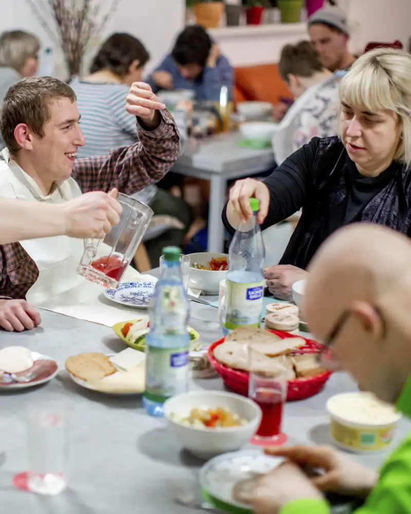 Frauen und Männern  mit und ohne Behinderung sitzen beim gemeinsamen Essen am Tisch.