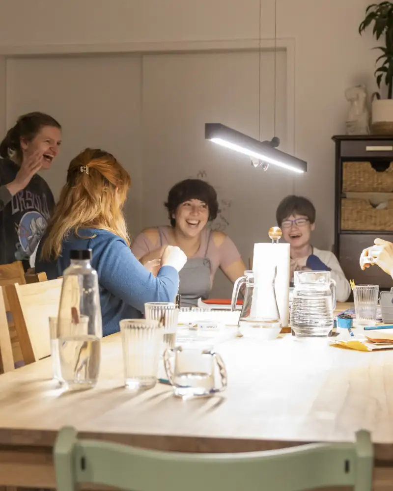Fünf junge Frauen lachen an einem großen Tisch.