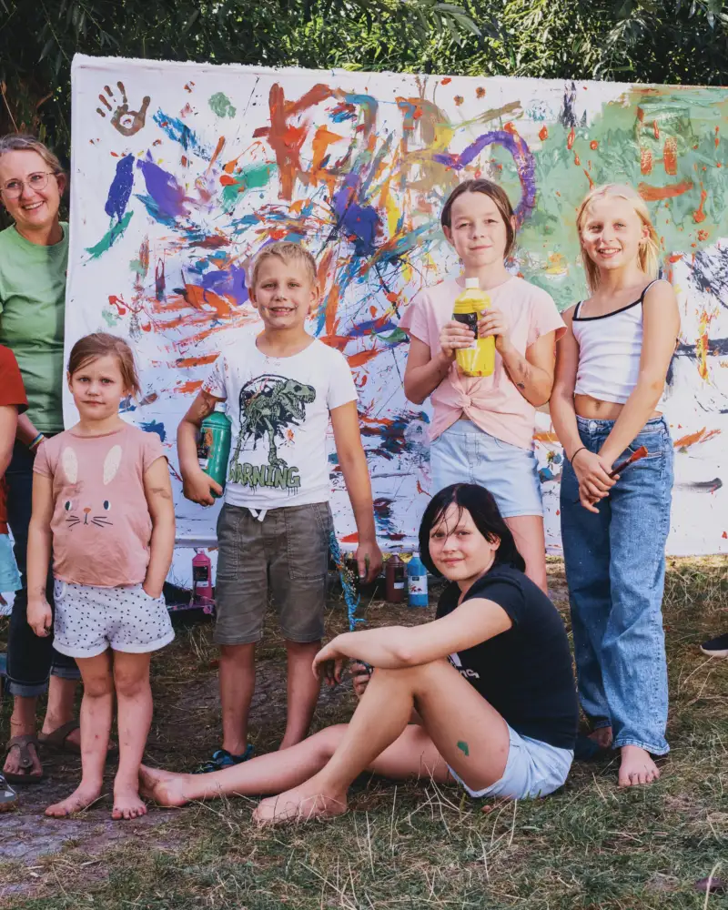 Eine Gruppe von Kindern in der Natur vor einem bunt bemalten Bild.
