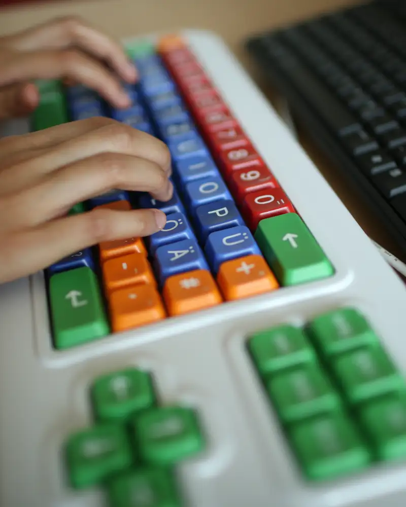Zwei Hände sind auf einer bunten Computertastatur zu sehen.