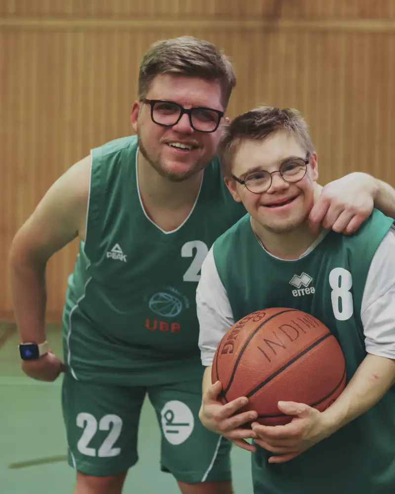 Drei Personen mit und ohne sichtbare Behinderungen in Basketballtrikots.
