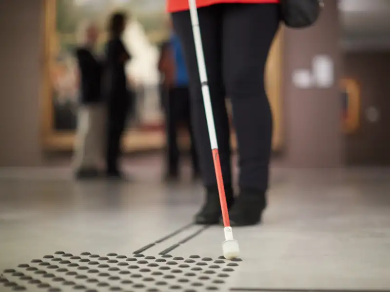 Eine Person orientiert sich mit Langstock an einem Blindenleitsystem