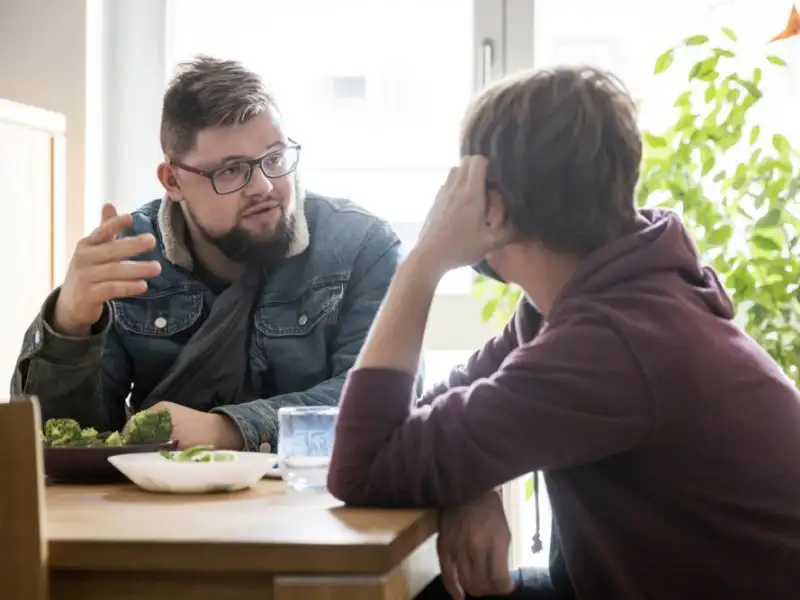 Zwei Männer sitzen an einem Tisch und sprechen miteinander.
