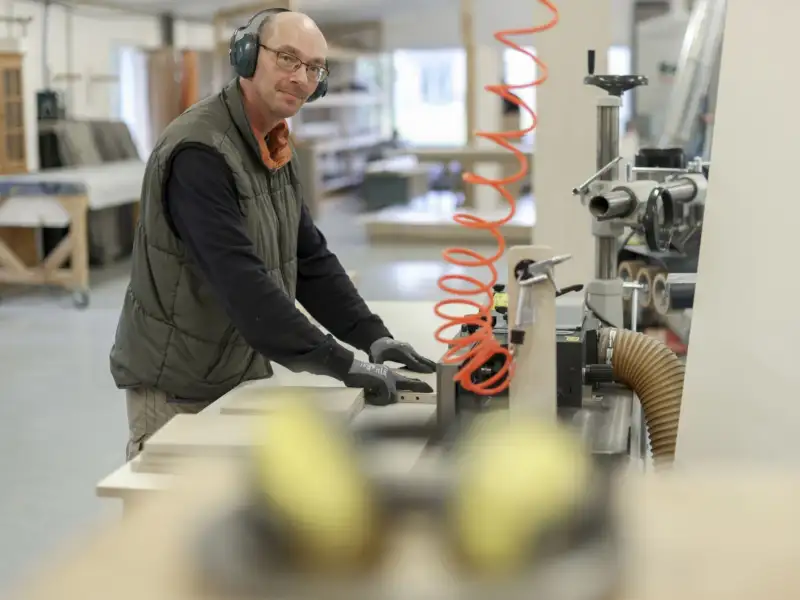 Ein Mitaarbeiter bei der maschinellen Bearbeitung von Holzbauteilen in der inkusiven Möbeltischlerei Hand in Hand-Werk Munster.