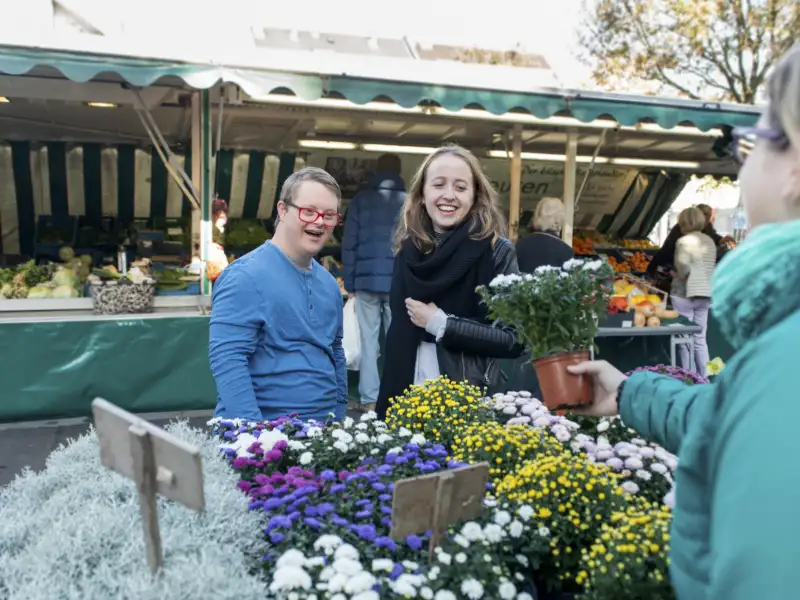 Ein junger Mann mit Downsyndrom und eine junge Frau schauen sich Blumen auf einem Markt an.