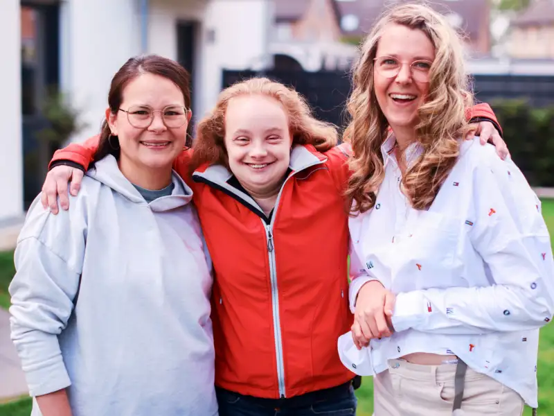 Drei Frauen stehen nah beieinander und lächeln.