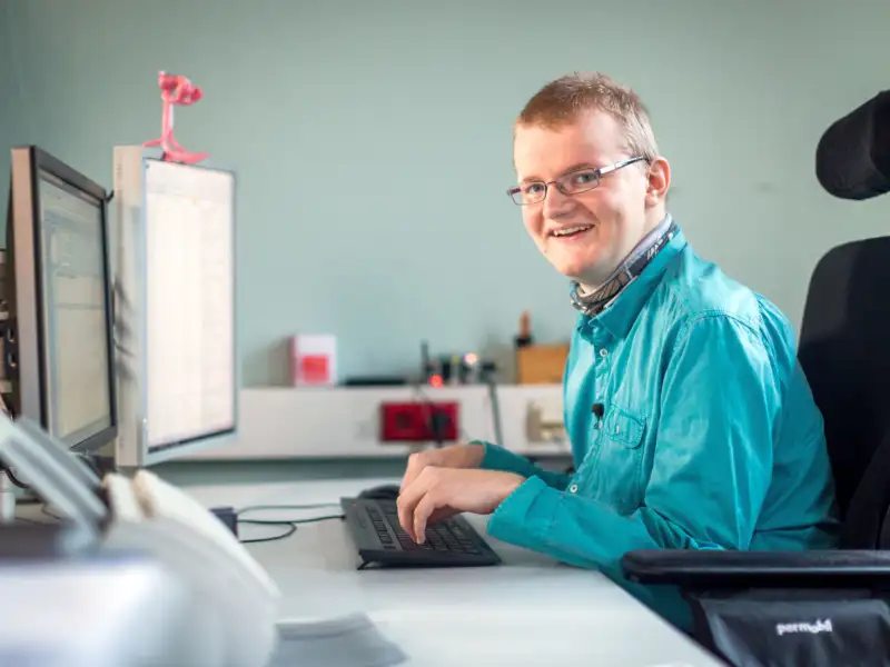 Ein junger Mann im Rollstuhl arbeitet am Computer