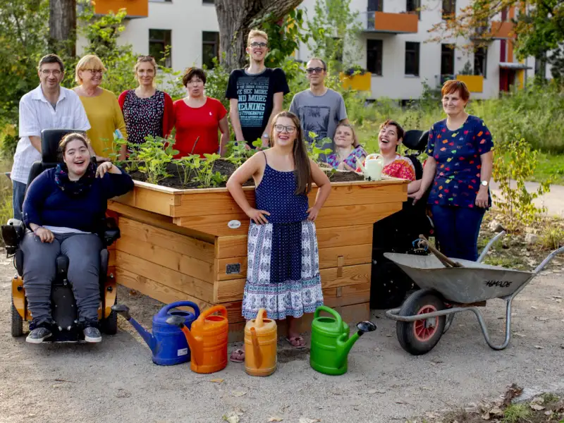 Eine inklusive Gruppe von Menschen steht um ein Hochbeet.
