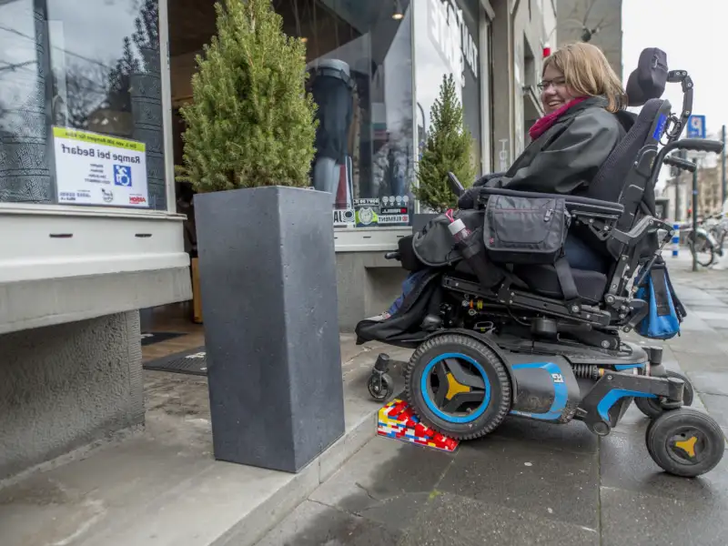 Eine Frau im E-Rolli fährt über eine Lego-Rampe in ein Geschäft.
