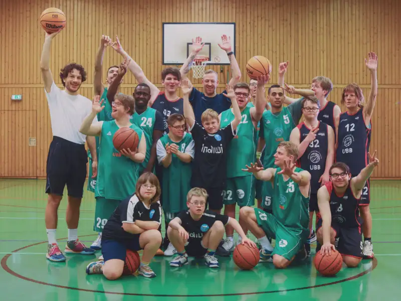 Eine inklusive Basketball-Mannschaft hebt die Hände in die Luft.