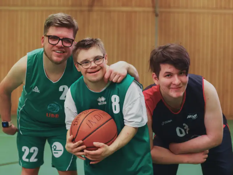 Drei Sportler:Innen mit einem Basketball