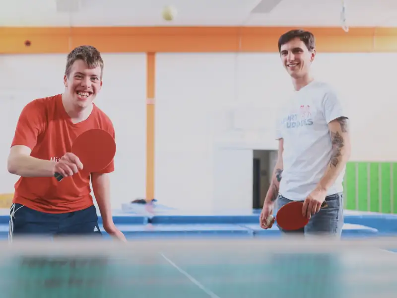 Ein Mensch mit Behinderung und einer ohne Behinderung spielen Tischtennis