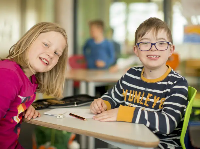 Ein Junge mit Behinderung und Mädchen in der Schule lächeln in die Kamera