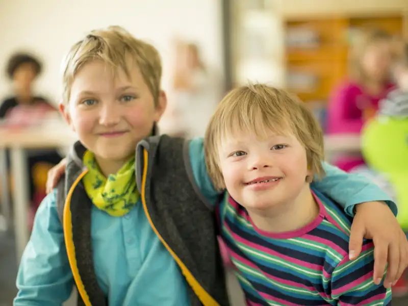 Zwei Jungs legen die Arme um die Schultern, einer hat das Downsyndrom